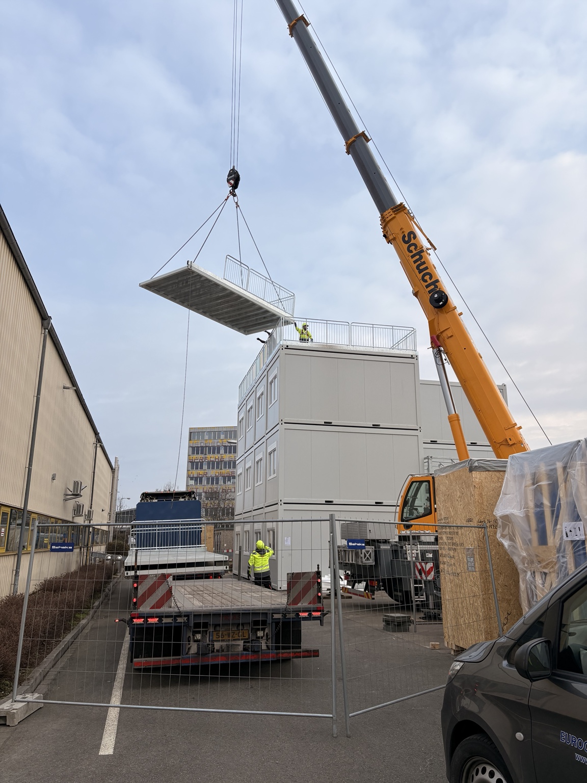 Mobilkran hebt eine Plattform mit Geländer an einer dreigeschossigen Containeranlage ein