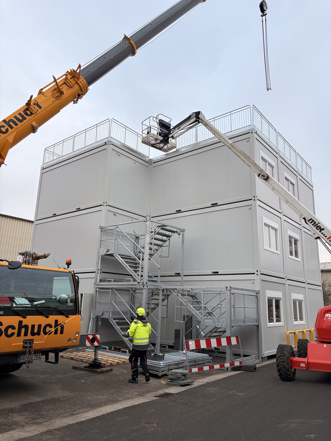 Mehrgeschossige Containeranlage während der Montage mit Außentreppe, Kran und Hubarbeitsbühne